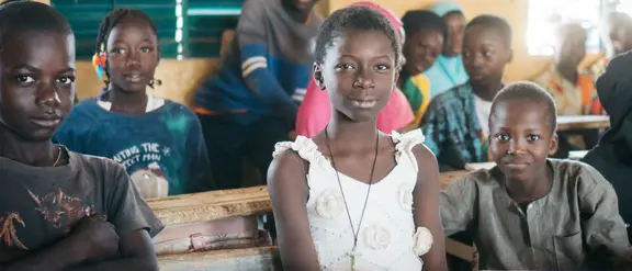  Kinder in einem Klassenzimmer in Burkina Faso sitzen lächelnd und aufmerksam an ihren Tischen.