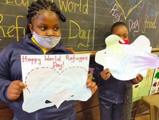 Südafrika: Aktion von Kindern zum Weltflüchtlingstag. Mädchen halten selbst gemalte Plakate hoch.