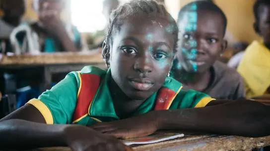 Ein aufmerksames Mädchen sitzt in einem Klassenzimmer in  Burkina Faso. Die Szene zeigt die Bedeutung von Bildung und die Hoffnung auf eine bessere Zukunft durch Lernen.