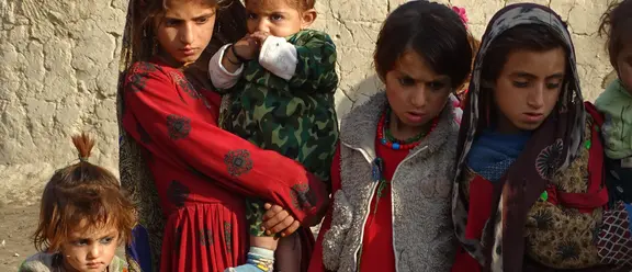 Eine Gruppe von Kindern in bunter, traditioneller Kleidung steht vor einer lehmigen Wand.