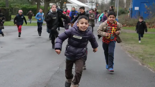  Flüchtlingskinder in Deutschland rennen lachend im Freien und genießen ihre Freizeit.