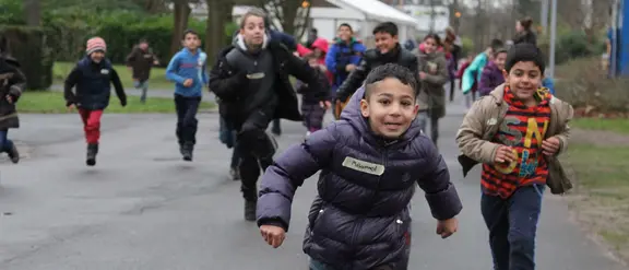  Flüchtlingskinder in Deutschland rennen lachend im Freien und genießen ihre Freizeit.