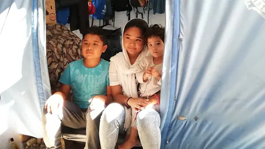 Drei Kinder sitzen im Eingang eines Zeltes in einem Flüchtlingslager in Griechenland, vereint in ihrem Zusammenhalt.